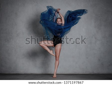 Young modern dancer in blue dress. trains and dances in a gray studio Royalty-Free Stock Photo #1371197867