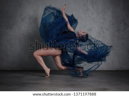 Young modern dancer in blue dress. trains and dances in a gray studio Royalty-Free Stock Photo #1371197888