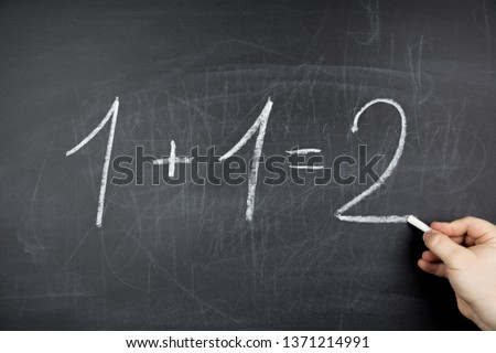 One plus one equals two written on black chalkboard. Drawn in chalk in a man's hand Royalty-Free Stock Photo #1371214991