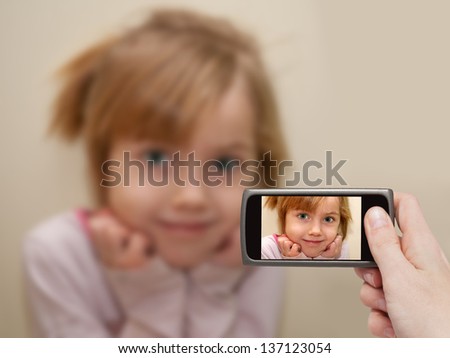 Man's hand making photo of a little girl with a mobile phone. Selective focus on a mobile phone with a portrait of a girl.