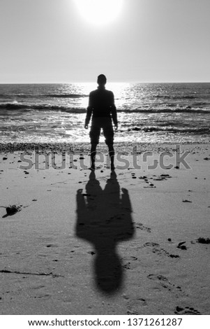 Silhouette of man and shadow standing on beach black and white. Loneliness and solitude concept. Men silhouette on sea background monochrome. Peaceful landscape with lonely person.