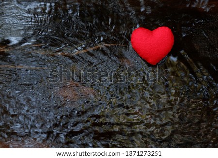 One red heart on a blurred brown textured wooden background with water flowing through. With copy space, top view.