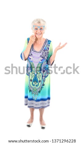 Pretty senior woman smiling and doing a hand gesture to one side while holding blue glasses against a white background