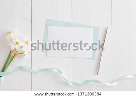 Mockup white greeting card and envelope with white daffodils on a white wooden table