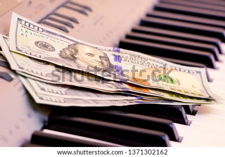 US Dollars lie on the piano keys. Payment for the concert, profit from performing musical works