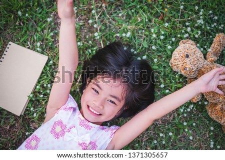 Portrait of adorable kid lying in beautiful green park. The lovely girl like playing outdoor & loves nature. Children likes having fun & read book in summer. Eco friendly & love nature concept.    