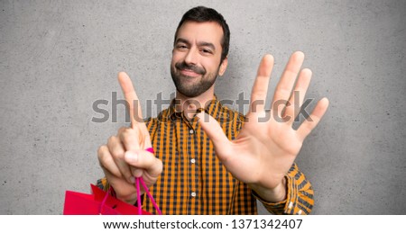 Man with shopping bags counting six with fingers over textured wall