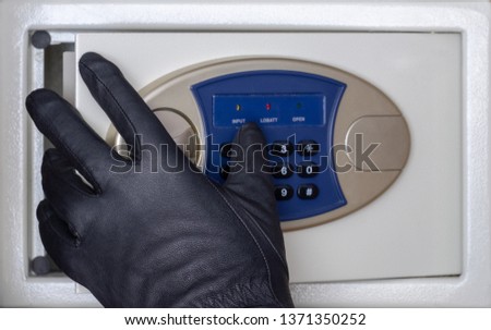 A black-gloved thief opens the safe door with a combination lock. Concept. Security at home, hotel and office. Theft of valuables and money.