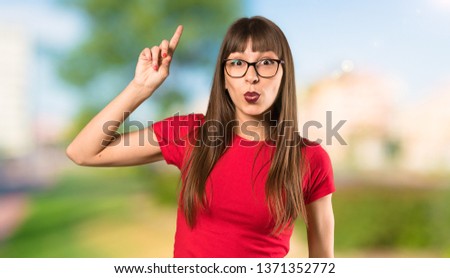 Woman with glasses intending to realizes the solution while lifting a finger up at outdoors