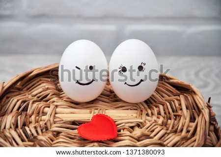 A loving couple of eggs with emoticons and a heart on a wooden basket. Congratulatory card with Easter.
