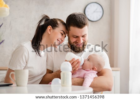Happy young couple feeding infant from bottle