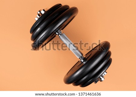 Professional dumbbell and weight plates over beige background. Black metal dumbbell with chrome silver handle. Gym equipment. Fitness concept.