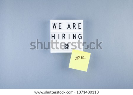 Creative top view flat lay of desk with we are hiring text on lightbox with copy space on blue background in minimal style. Concept of new job, hiring recruitment process, new team members screening