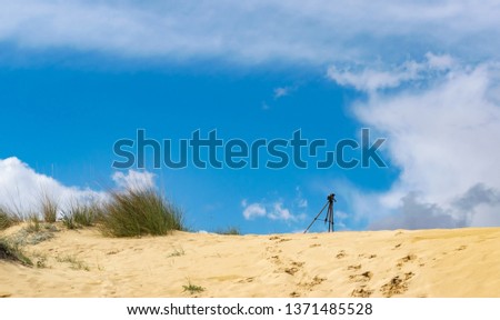 Tripod with smartphone on sand hills with grass and blue sky on background. Shooting time lapse video concept. Horizontal, space for text.