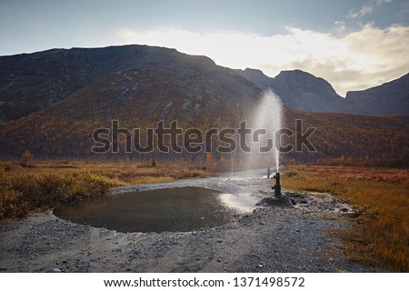 Geological well beats a fountain of water against the backdrop of mountains Royalty-Free Stock Photo #1371498572