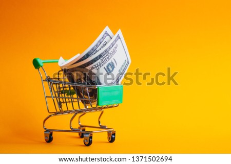 USA dollars in shopping cart, Shopping cart on orange background with money in it, one hundred dollars in shopping cart