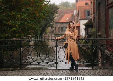 Stylish woman in brown coat standing on the bridge in Bealgium, Brugge. Female put on a hood