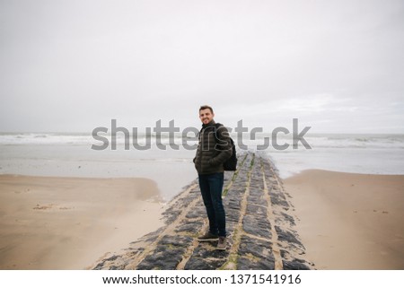 Male tourist walkin along the North Sea. Man with backpack stand on the coast in rainy weather. Beautiful sea
