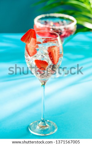 Summer cocktail concept: Icy gin fizz with fresh strawberries on turquoise background with palm leaves shadows