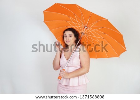 feminine woman with plus size body in pink dress with orange big heart shaped umbrella posing on white background in Studio