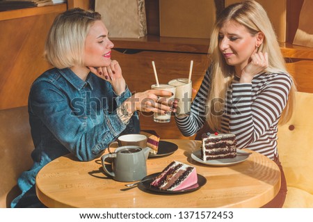 Two happy women sitting in a cafe, drink a cocktail, tell each other funny stories, being in a good mood, laughing happily. Best friends