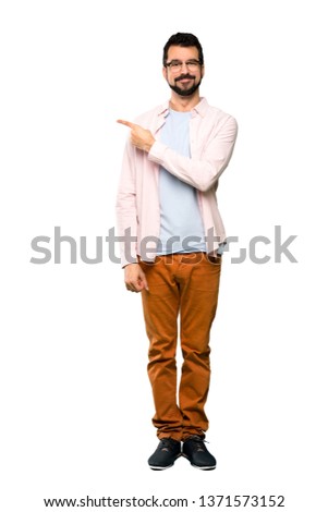 Full-length shot of Handsome man with beard pointing to the side to present a product over isolated white background