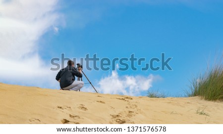 Man setting up mobile phone on tripod for photography and video making in sand hills. Cloudy sky on background. Travel photographer concept.