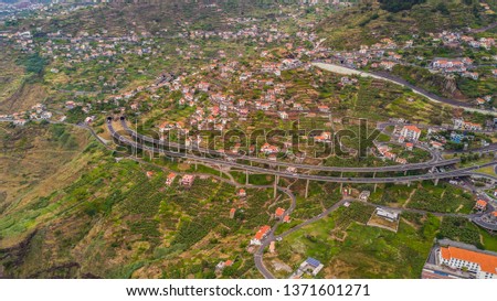 Aerial panoramic cityscape view of the cities in madeira with houses in front of tree covered mountains and white clouds