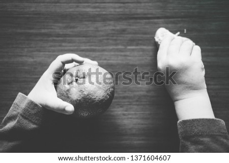 Black and white picture showing the hands of a kid, one grabbing a tangerine and the other grabbing a slice.