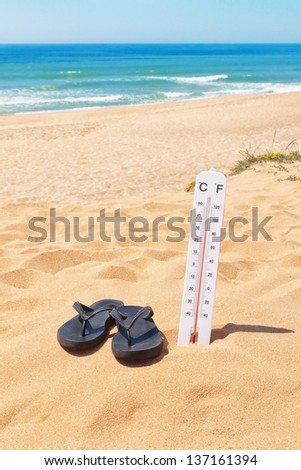 Slippers on the beach beside the thermometer and the sea. Summer.