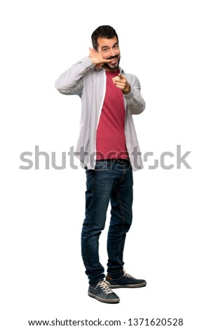 Full-length shot of Handsome man with beard making phone gesture and pointing front over isolated white background