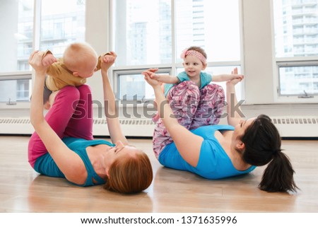 Group of two young women with children doing workout in gym class to loose baby weight. Child-friendly fitness for mothers with kids. Lifestyle concept of family activity for moms.