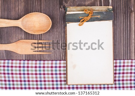 Recipe notebook, tablecloth, spoon, fork on wood texture background