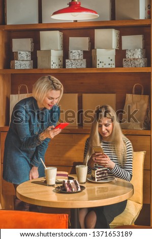 Two happy women sitting in a cafe and taking selfies on the phone, drink a cocktail, tell each other funny stories, being in a good mood, laughing happily. Best friends