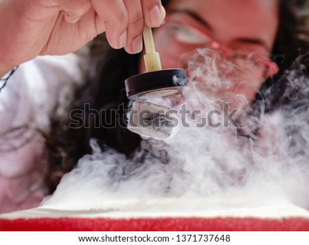 Female Student Demonstrates Quantum Magnetic Levitation and Suspension Effect. A splash of liquid nitrogen cools a ceramic superconductor forcing it to float in air below a magnet Royalty-Free Stock Photo #1371737648