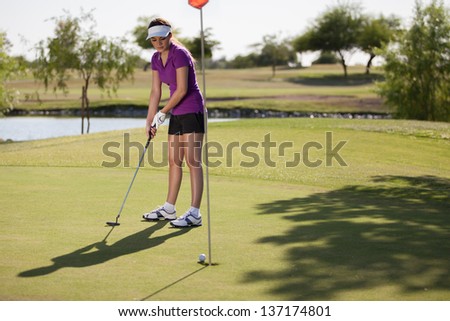 Gorgeous female golfer putting in the green on a sunny day