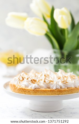 Lemon meringue pie on a white cake stand and yellow tulips