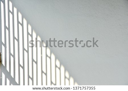 Pattern of shadow of fence on white wall in soft focus and dark light, background of backdrop half plain of picture and half have shadow, minimal image create from sun light, abstract concept