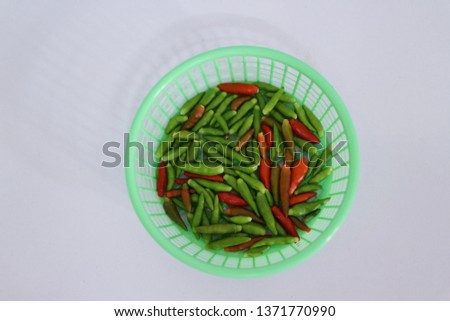 Close-up pictures of small red and green peppers, vegetables, herbs in a green basket, white background