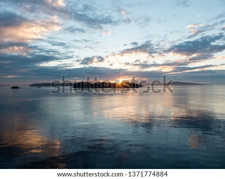 Sunrise or sunset on the Pacific West Coast with a calm seas, islands and variety of clouds herald the start or end of a new day. A serene seascape background. 