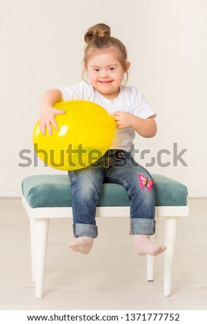 Beautiful girl with down syndrome sitting in a chair and playing with a balloon, isolated on white background