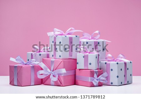  Many gift boxes on delicate pink background. Stylish modern gifts of pink and white paper, decorated with pink satin ribbon with bows. Holiday concept, copy space.