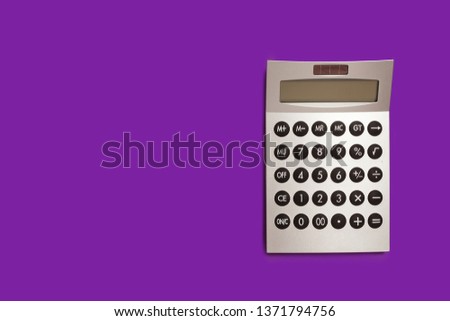 grey plastic calculator lying isolated on a purple background. back to school concept. free space for text