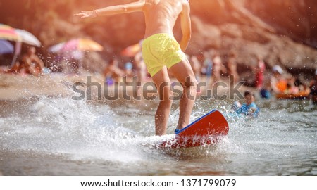 Male athletic legs close up.Young man beginner surfer in yellow shorts learns to catch wave on shore red Board. Background is blurred