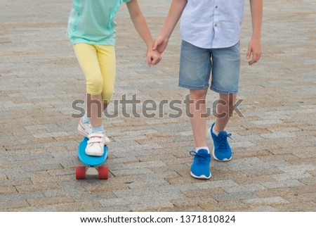 the boy holds the girl's hand, teach skating on a sports Board, legs close-up, on the background of stone blocks