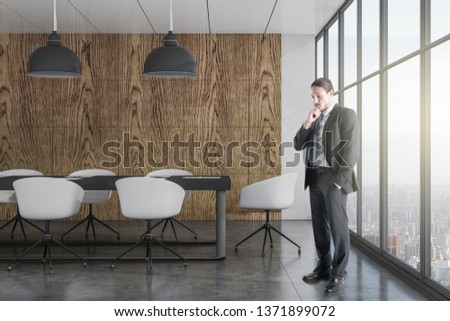 Attractive young european businessman standing in luxury coworking office interior. Research and boss concept.