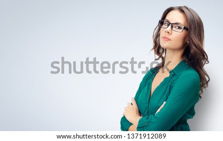 Picture of happy smiling young business woman in green confident clothing and glasses, with empty copy space place for some text, advertising or slogan, over grey background