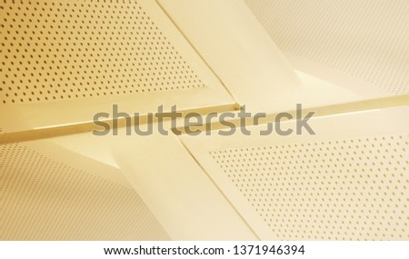 Perforated ceiling panels. Fragment of modern office architecture interior. Diagonal geometric compostion with polygonal structure in light yellow halftones.