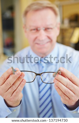 Happy smiling senior optician holding new glasses at consultation Royalty-Free Stock Photo #137194730