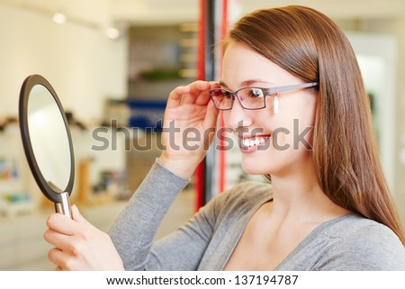 Young woman checking her new glasses in a mirror at optician retail store Royalty-Free Stock Photo #137194787